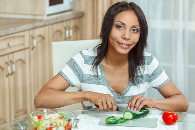 Beautiful woman slicing cucumber for salad in modern kitchen