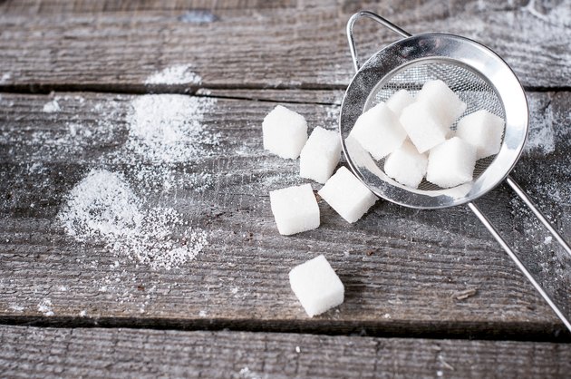 Lump sugar in a metal strainer s on wooden background.