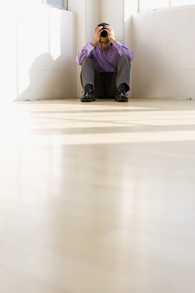 Businessman sitting on floor in corner with head in hands
