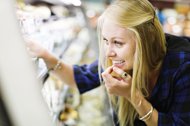 Beautiful blonde shopper checks supermarket fridge contents, smiling