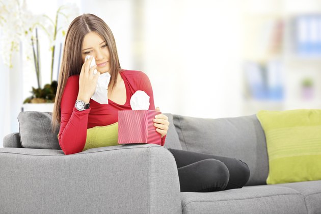 Sad female seated on sofa wiping her eyes
