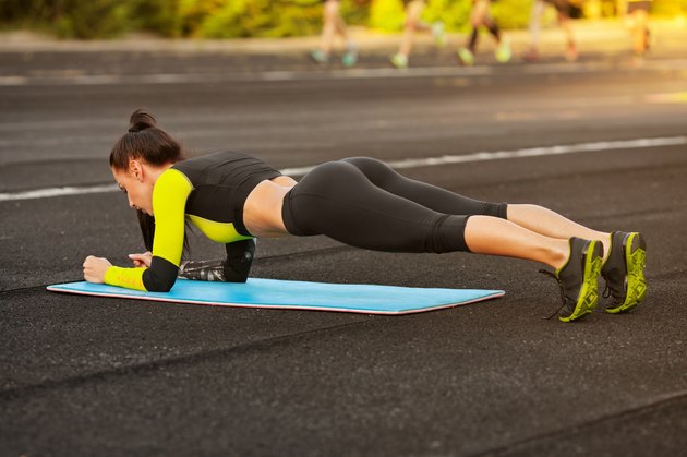 Slim athletic woman doing planking exercise in the stadium, outdoors