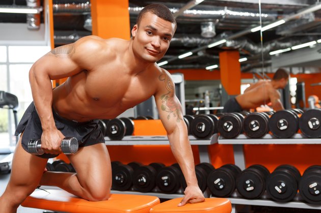 Muscular man doing exercises with dumbbells in gym