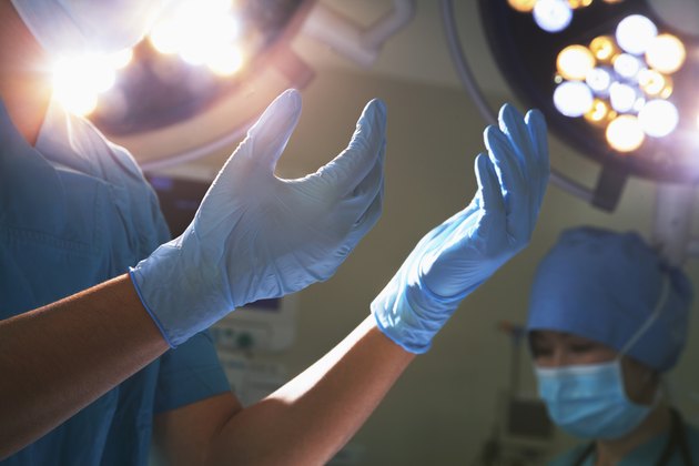 Midsection view of hands in surgical gloves and lights