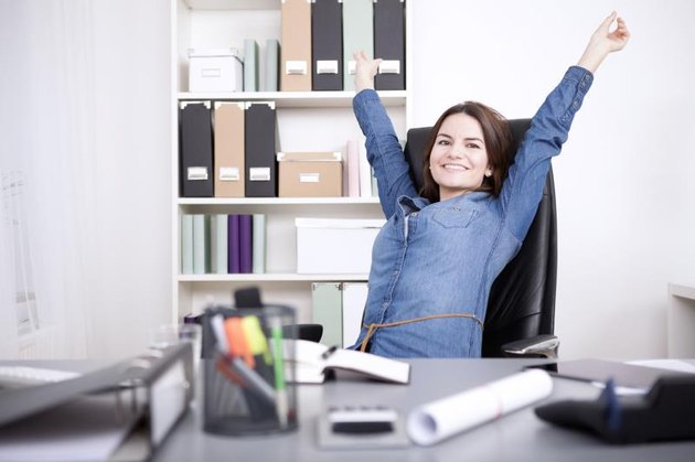 Happy Young Office Woman Sitting on her Chair Stretching her Arms While Looking at the Camera.