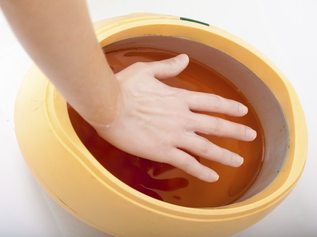 Female hand orange paraffin wax bowl. Manicure beauty spa salon