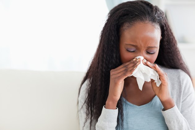 Close up of woman blowing her nose on couch