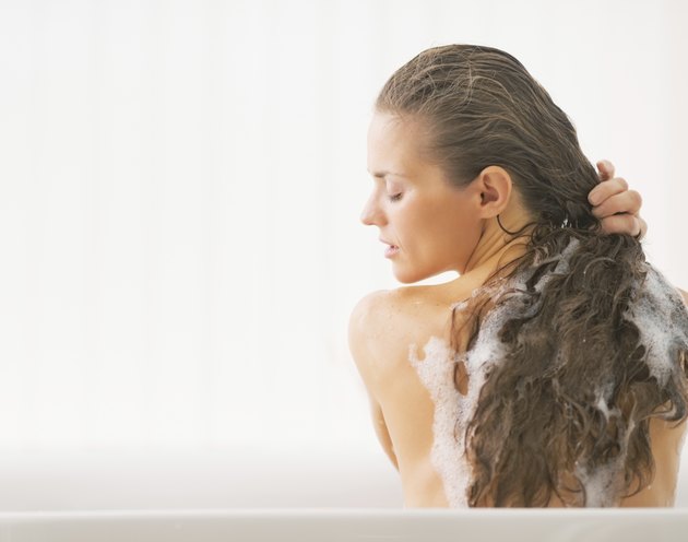 young woman washing hair in bathtub