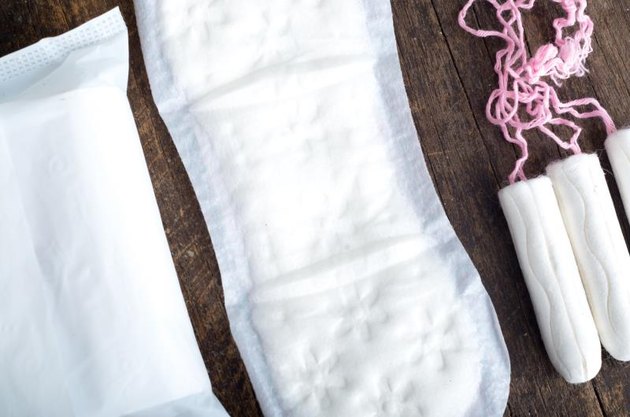 Sanitary pads for women with clean white tampons lying on top of wooden surface, shot from above angle.