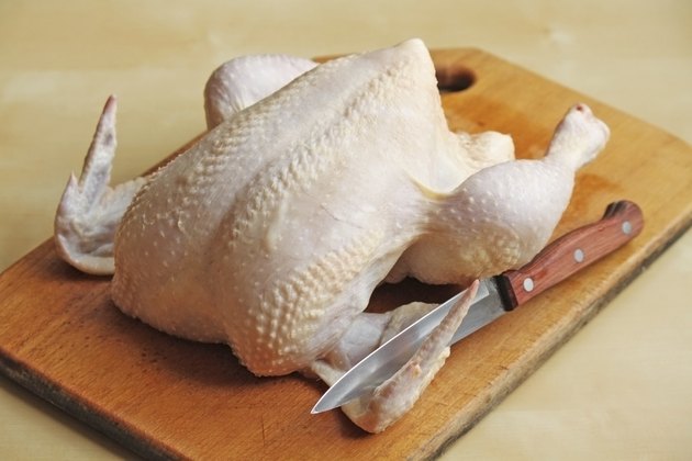 Whole raw chicken on the chopping board with a knife