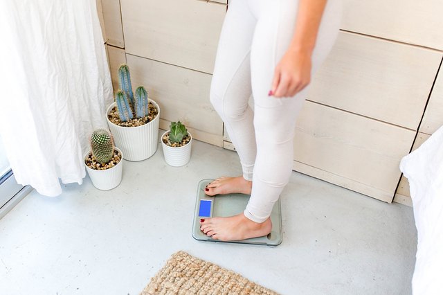 Woman standing on bathroom scale, weighing herself and tracking weight-loss progress