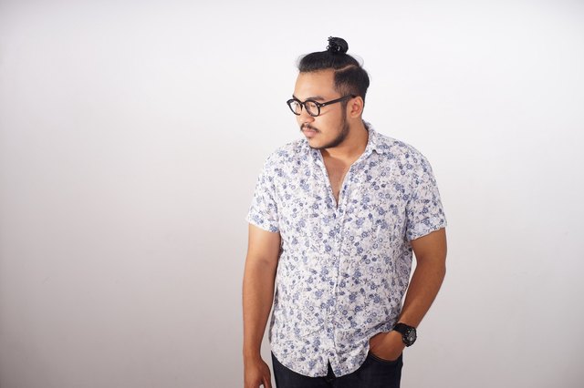 man with man bun poses against wall