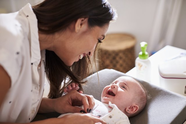 Happy four-month-old baby boy lying on changing table looking up at his mum, close up