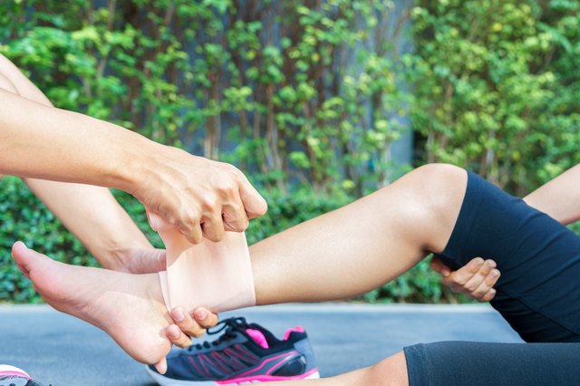 Woman runner ankle being applied bandage by man in park. injury ankle