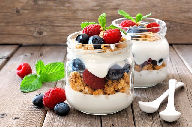 Blueberry, raspberry parfaits with yogurt in mason jars, still life against wood