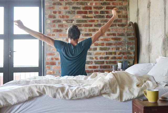 Rear view of young man stretching hands in bed