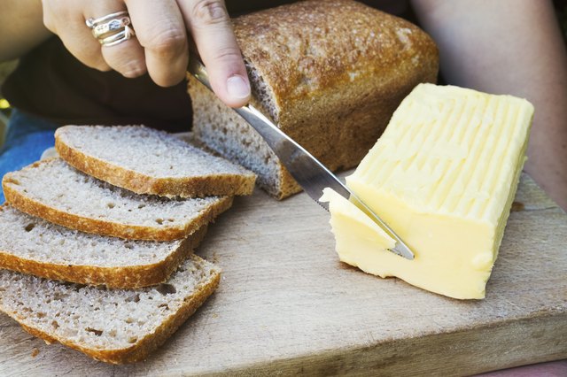 A person with a knife slicing through a block of butter for a sliced bread loaf