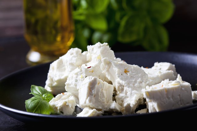 Feta, herbs and basil leaves on black plate, closeup