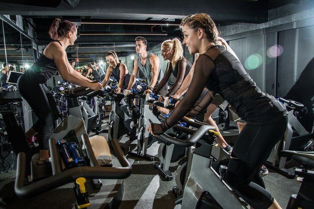 Group of sporty people with their instructor training on cycling class in gym