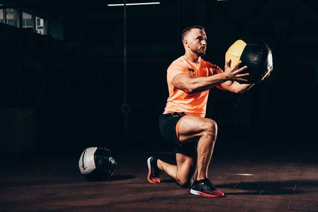 handsome athletic sportsman performing lunge with medicine ball in dark gym