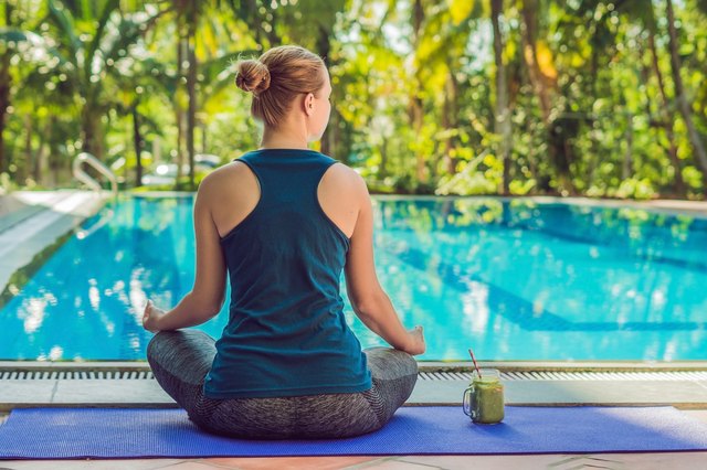 Closeup of a woman's hands during meditation with a green smoothies of spinach, orange and banana on the background of the pool
