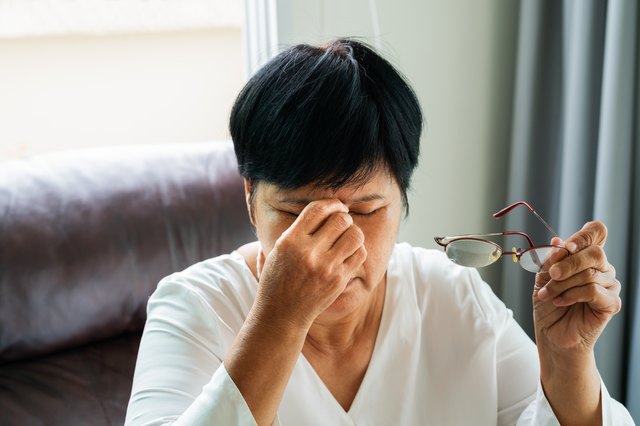 女人摘掉眼镜，在看完纸质书后按摩眼睛。因长时间戴眼镜感到不适，头晕