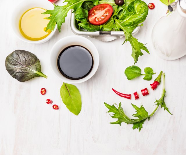 Salad preparation with oil and balsamic vinegar on white wooden