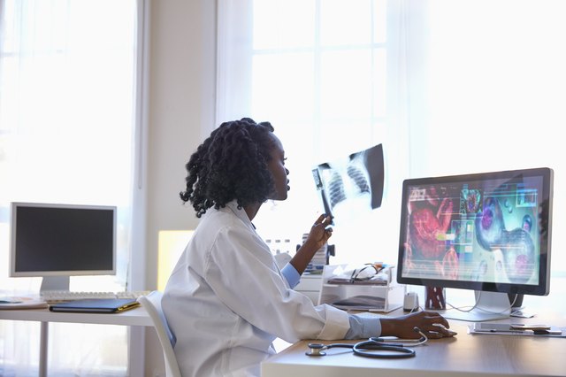 Black doctor examining chest x-ray and using computer