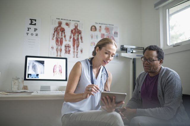 Female doctor with digital tablet talking with senior male patient in examination room
