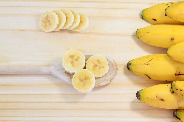 peeled banana on wood, sliced on wooden spoon, next to banana bunch, top view