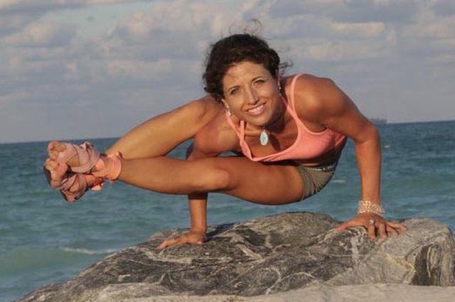 Young woman balancing on rock, practicing yoga pose, rear view