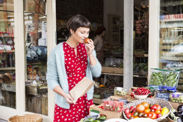 Woman smelling fresh tomato at organic farm shop.