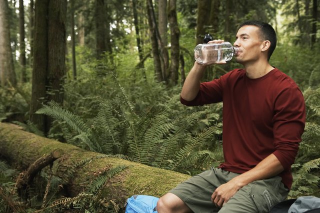 Young man sitting on log in forest, drinking water