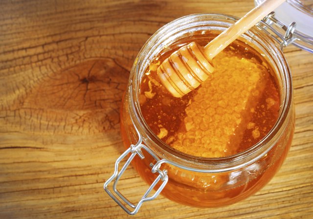 Jar of honey with honeycomb and dipper on wooden background