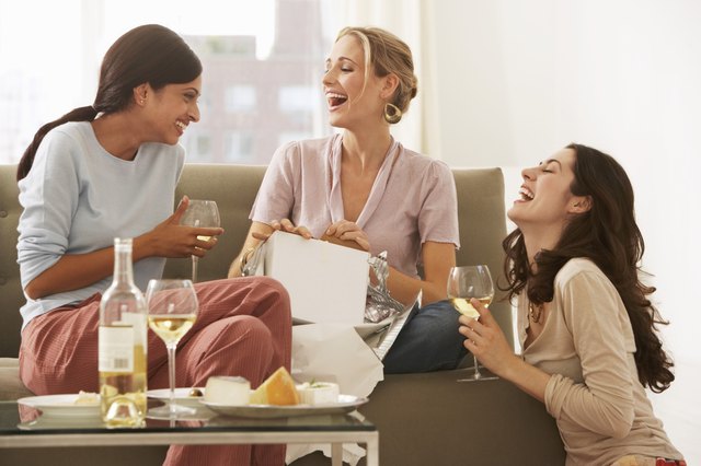 Three young women gathered on sofa, drinking wine and laughing