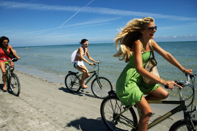 Three young woman riding bicycles on beach, laughing, side view