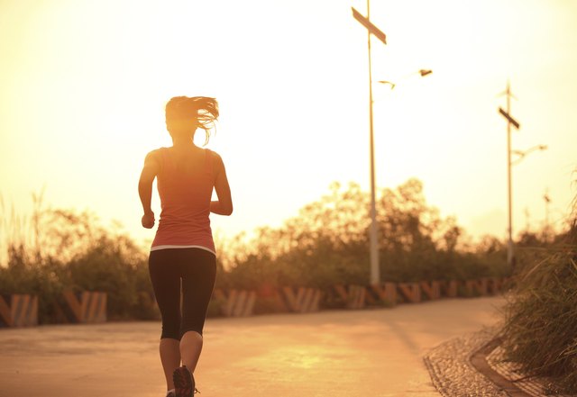 sporty woman morning exercise running on mountain driveway under sunrise