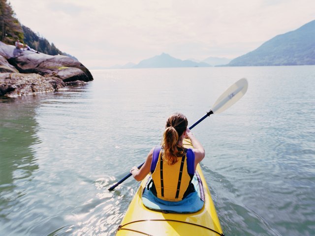 Woman kayaking, swinging paddle in air, rear view