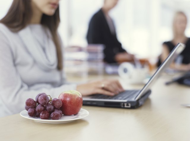 Young woman sitting at desk using laptop with grapes and apple