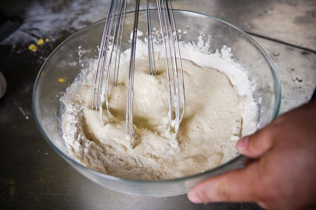 Baker beating eggs and flour in glass bowl