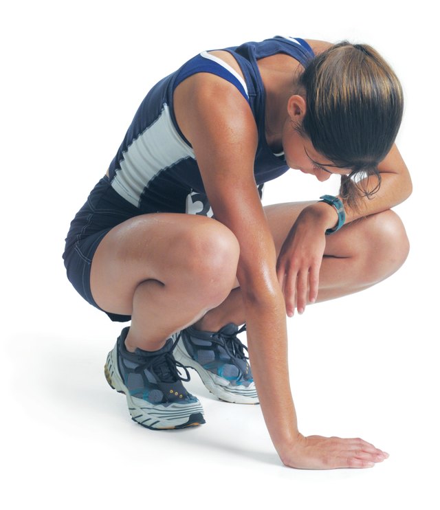 a young woman in a blue track uniform is squatting down as she leans against her knee and looks down