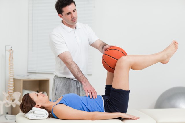 Physiotherapist placing a ball between the knees of woman
