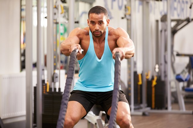 Young man working out with battle ropes at a gym