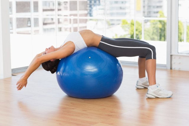 Fit woman stretching on exercise ball at gym