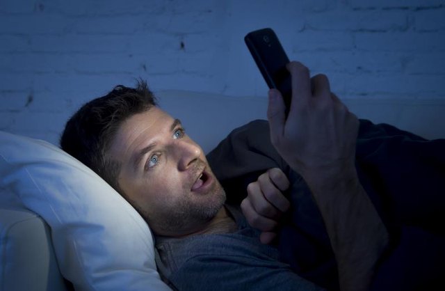 A young man watches porn on his phone in bed.