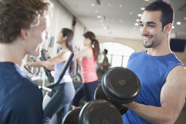 Two young men smiling and lifting weights in the gym