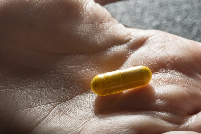 Bare hand holding one yellow medicinal tablet