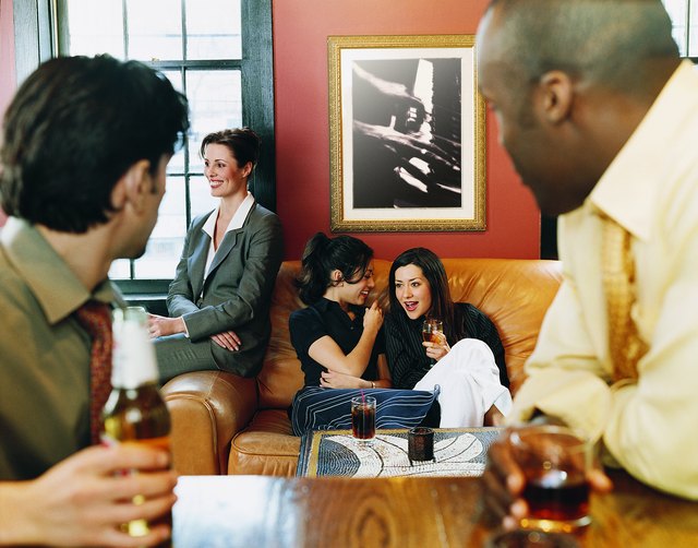 Businessmen Sitting at a Bar Watching Businesswomen Sitting on a Sofa
