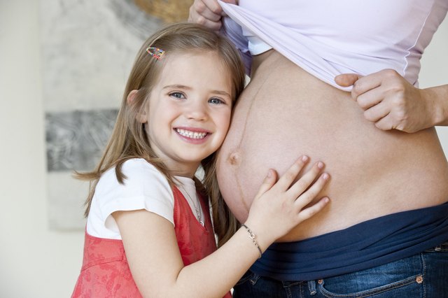 Daughter listening to pregnant mid adult mothers belly, smiling