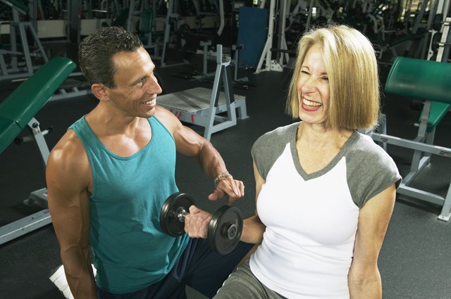 Male fitness instructor training senior woman in gym, smiling